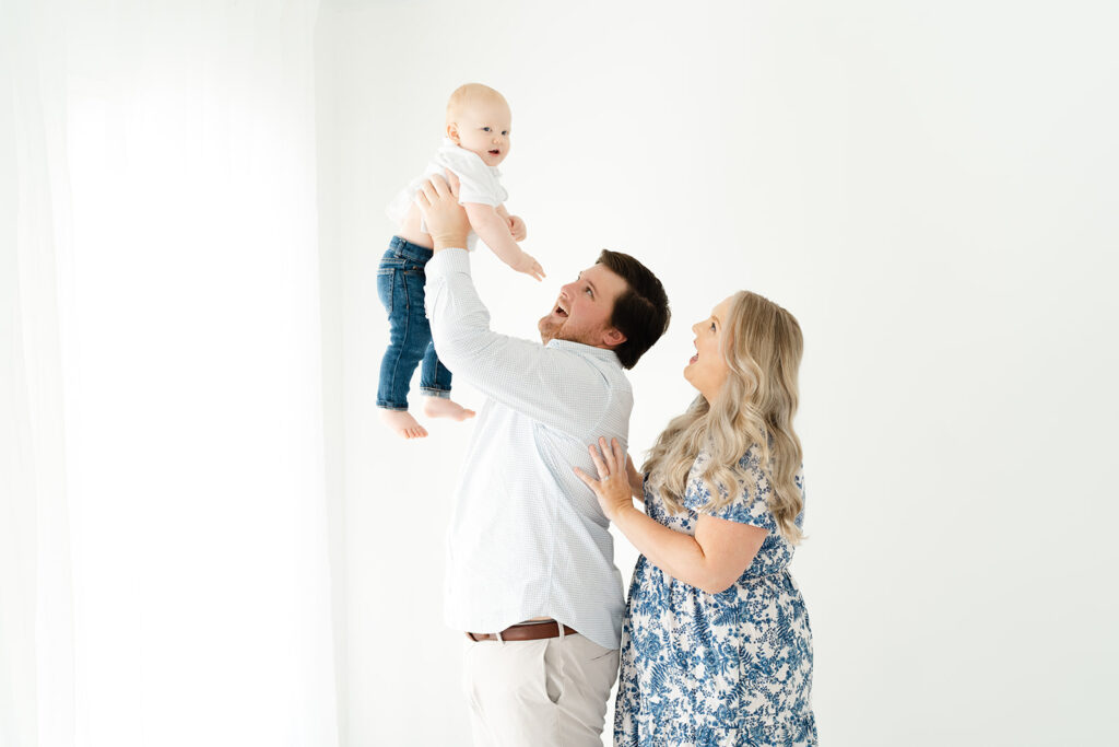Dad throwing baby in air mom behind in Marietta, GA studio by Lindsey Powell Photography