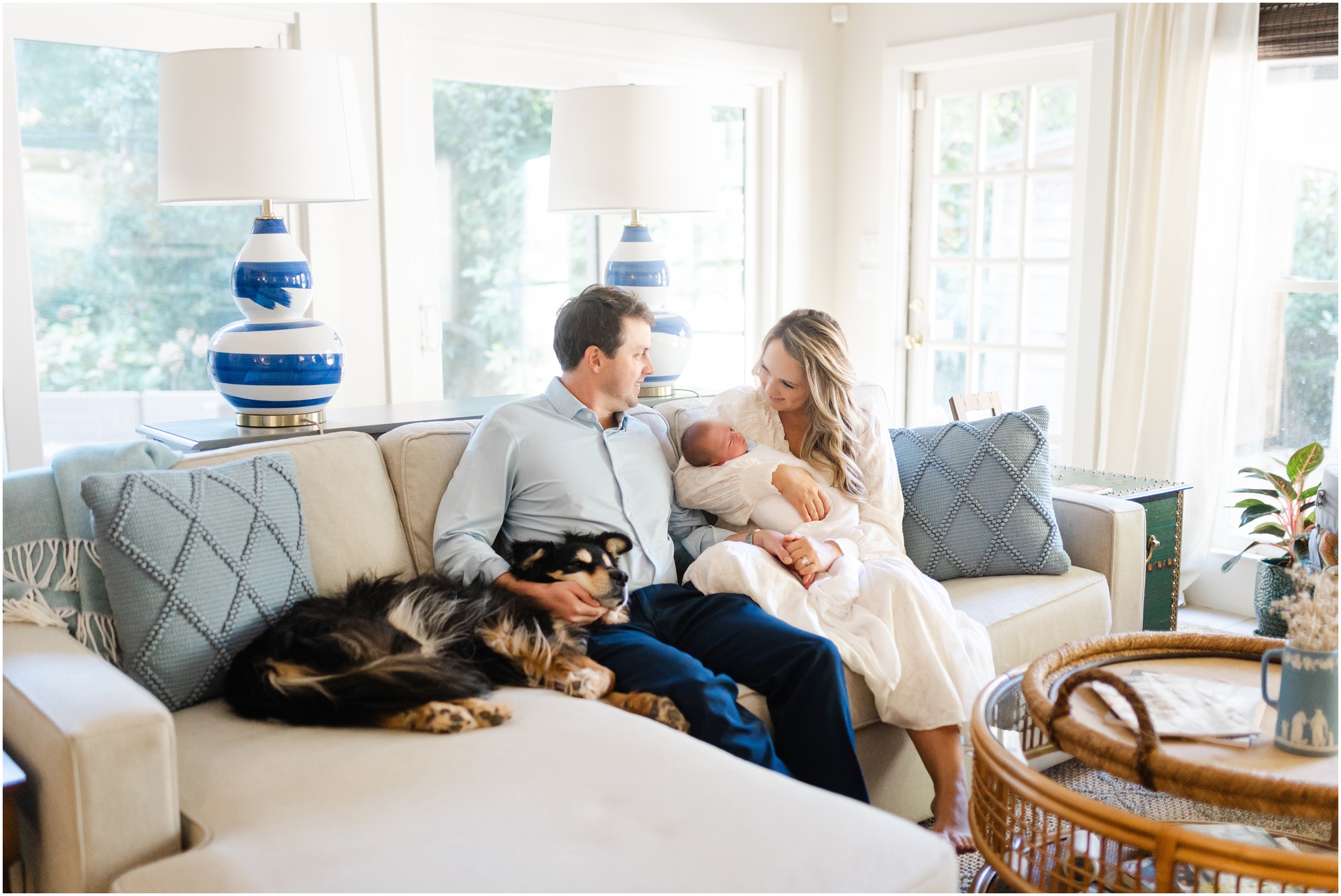 New parents sit with their dog and newborn baby on their couch during their Atlanta newborn photography session.